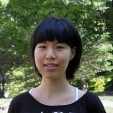 Woman with short black hair smiles in front of trees