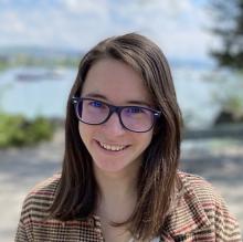 Woman with brown hair and glasses in front of a lake.