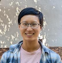 Woman with short black hair and glasses smiles in front of a white background