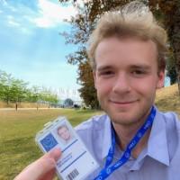 Man with ID badge smiles in front of sunny day