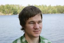 Man with brown hair in front of a lake.