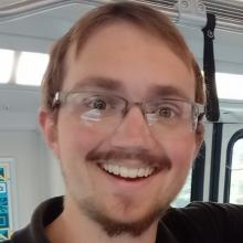 Man with brown hair and beard with glasses smiling at the camera.