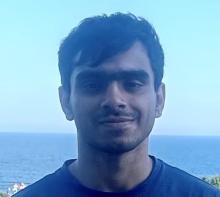 Man with brown hair and brown eyes smiles in front of the ocean