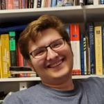 Man smiles in front of bookshelf